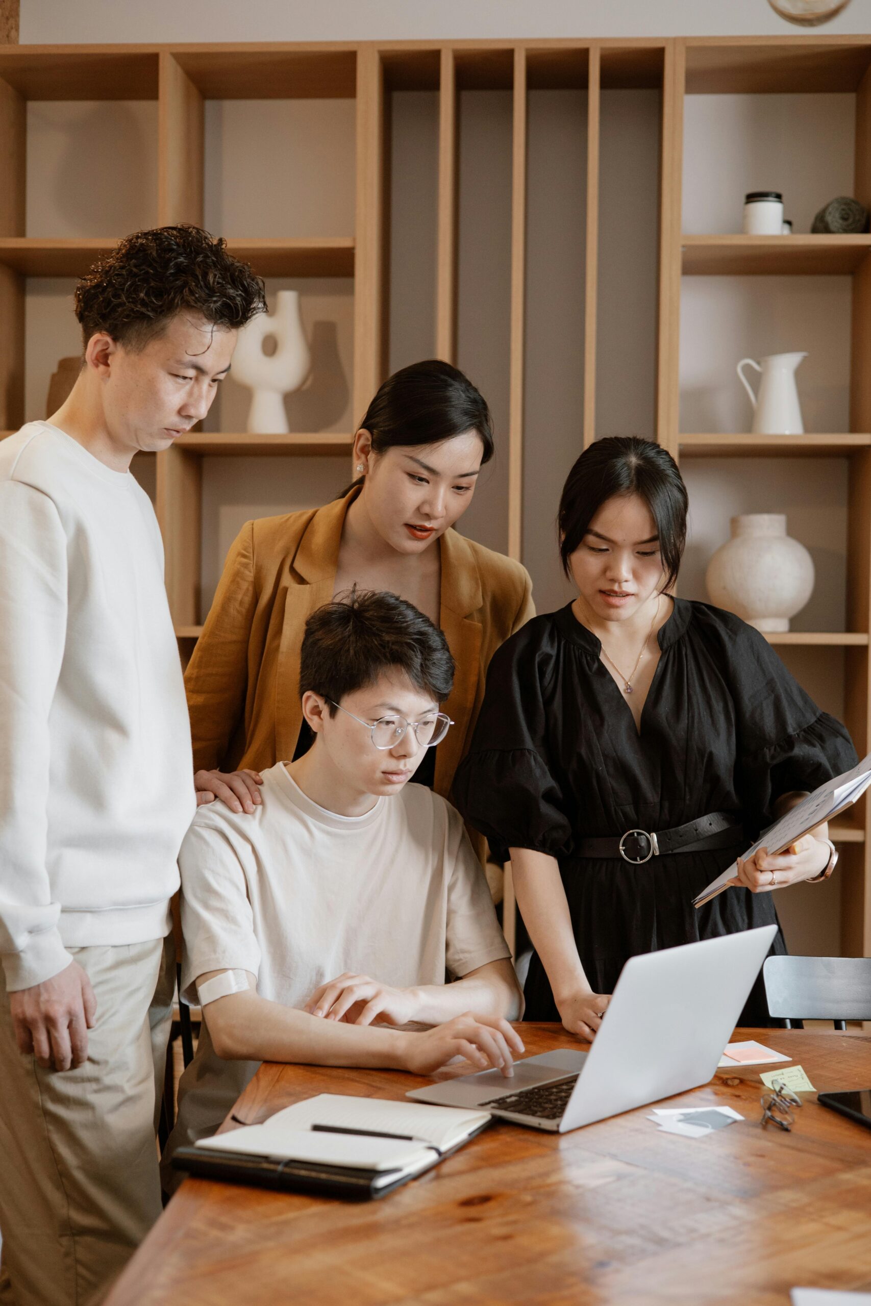A group of Asian professionals engaged in collaborative work around a laptop in an office setting.